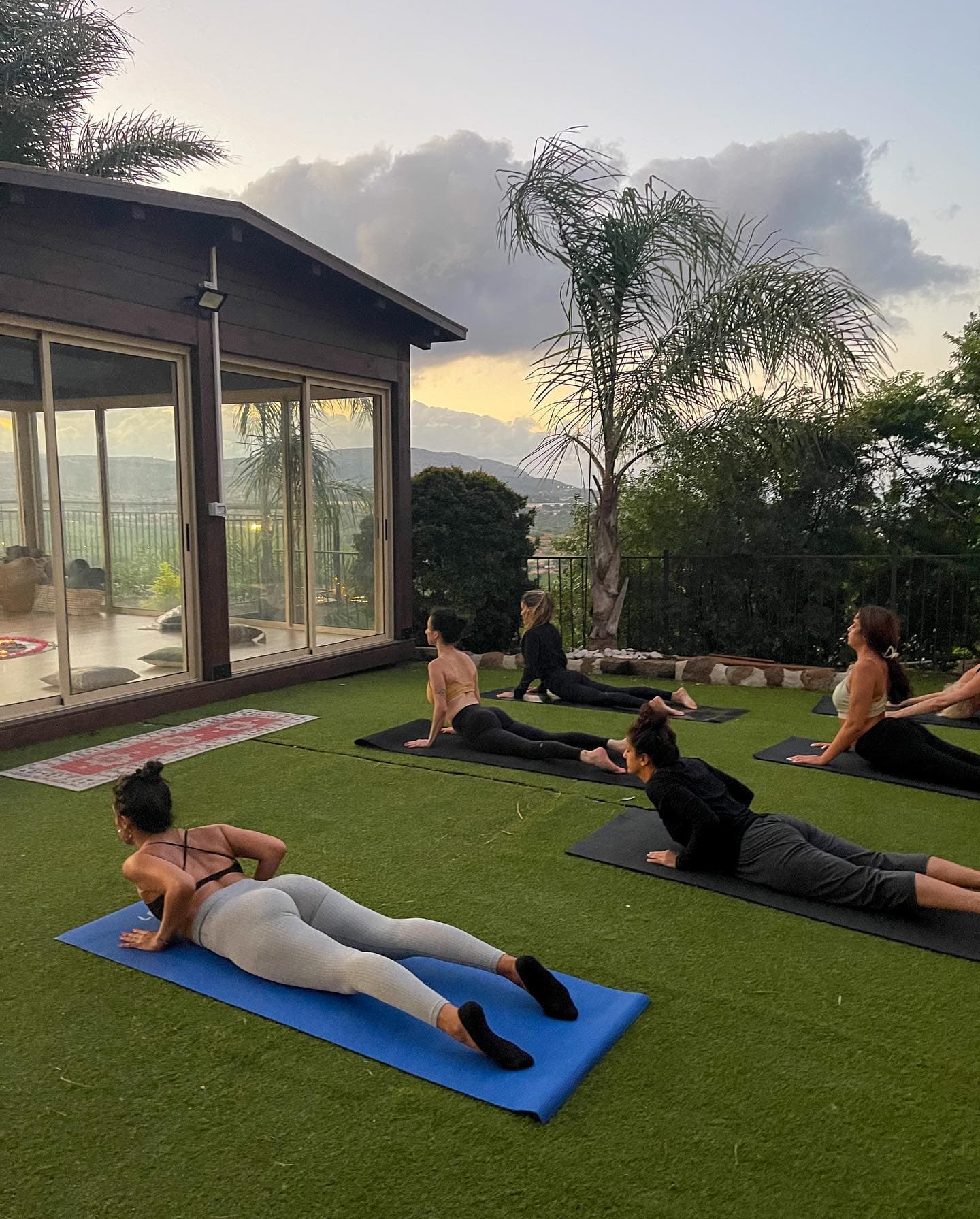 קבוצת יוגה על טרסה עם נוף הרים בשקיעה